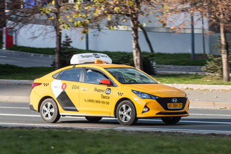 Moscow; Russia - October 14; 2021: yellow Hyundai Solaris   Yandex taxi is driving fast on the street on a warm autumn day against the backdrop of a  parkのeditorial素材