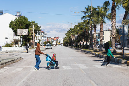 Cheerful family mother with a child in a stroller and a schoolchild are walking along a footpath in...