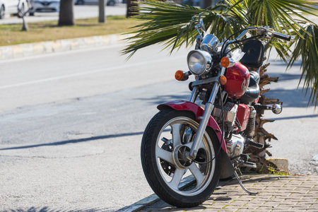Side, Turkey -January 19, 2022: A red motorcycle stands in a parking against the backdrop of street, green trees on a warm summer day . front viewのeditorial素材