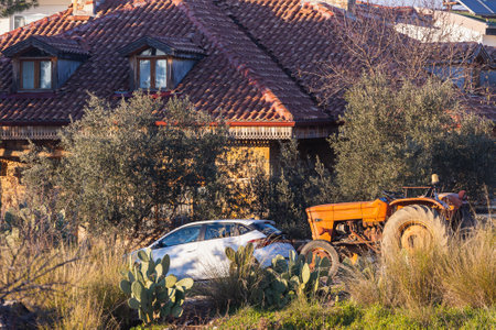Side, Turkey -January 28, 2022: a gray hatchback and an orange old tractor stand in the yard of an old house with a tiled roof in one of the village yards in Turkeyのeditorial素材