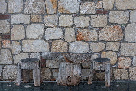 Close-up of a wooden table and chairs made by hand from stumps for outdoor recreation against the background of a stone wallの写真素材