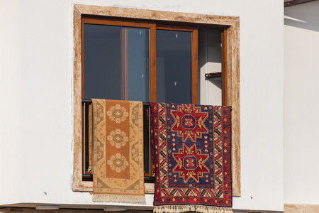Carpets with oriental ornaments are dried on the window of a snow-white house in Turkey.