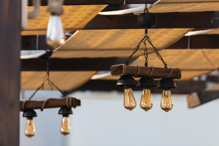 close-up of a candlestick from a wooden stick-beam and light bulbs in a loft style in an outdoor...