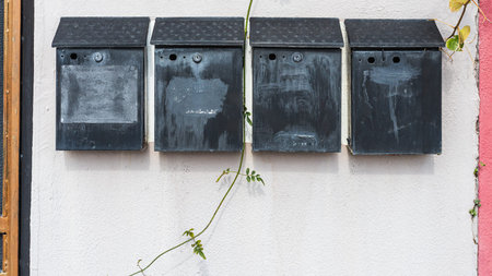 Close-up row of four black metal mailboxes on a white stone building