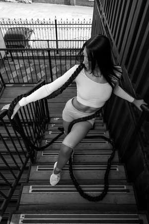 Outdoor close-up portrait of a young beautiful woman in sportswear with a rope, posing against the backdrop of an industrial container. sport lifestyle concept.の写真素材