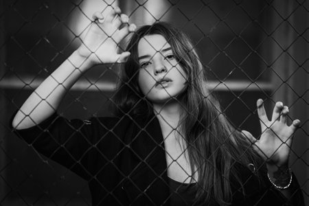 portrait Young dark-haired woman who stands behind a mesh fence in the distance. The concept of a...
