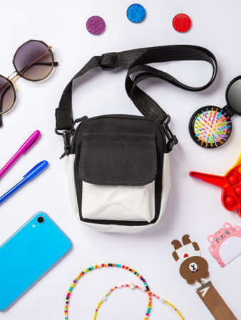 Flat lay photo of baby bag with cosmetics, cosmetics and smartphone, pop it toys, key chain sunglasses top view of basic beauty items for girlの写真素材