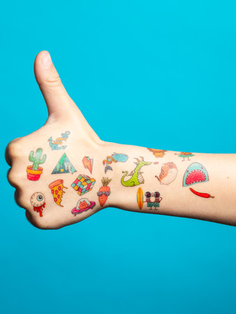 Thumb up of the hand of a little boy with a lot of transfer multi-colored tattoos on a blue isolated backgroundの写真素材