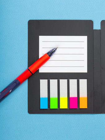Design concept - top view of notepad with white sheets, bookmarks, binder and pen on blue background...