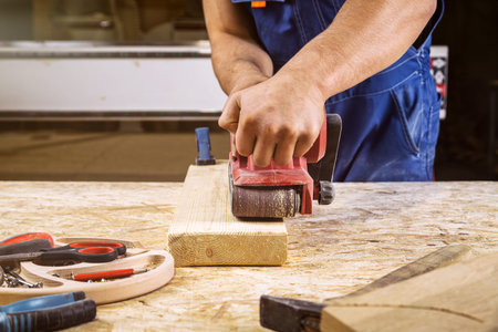Experienced carpenter in work clothes and small buiness owner working in woodwork workshop, using...