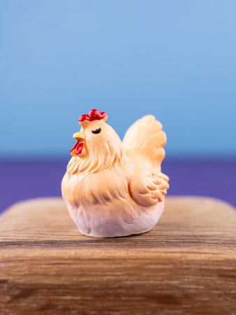 Close-up of a small, cute figurine in the shape of a chicken with a red comb, placed on a wooden podiumの写真素材