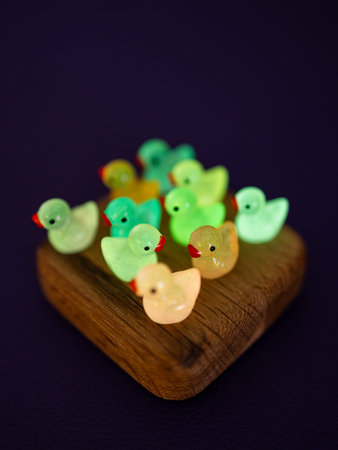 Close-up of a group of small, glowing, fun figurines of multicolored ducks on a wooden podium