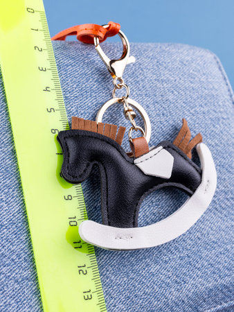 Close-up of a fashionable black leather horse keychain with a saddle, attached to a blue stylish bag