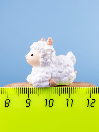 Close-up of a small, cute figurine in the shape of a white adorable lamb, placed on a wooden podium