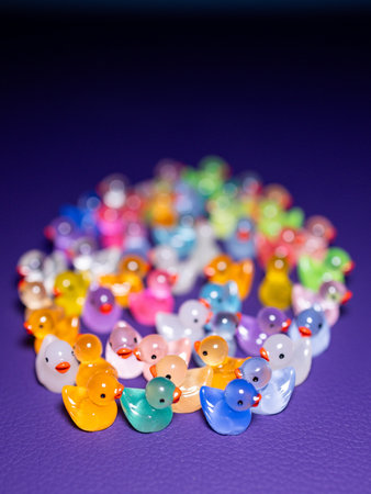 Close-up of a group of small, fun figurines of multicolored ducks on a purple backgroundの写真素材