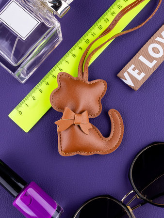 Close-up of a fashionable brown leather cat-shaped keychain with a bow on purple table with women...