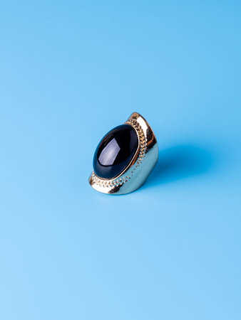 Close-up of a gold ring with a large black stone against a blue background