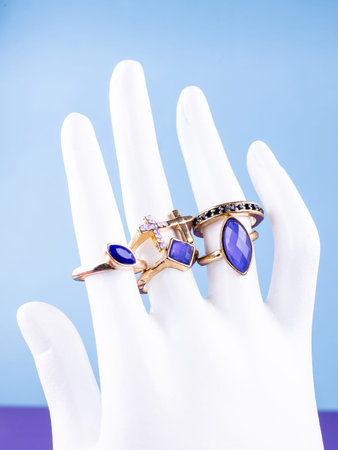 A close-up of a set of gold-colored jewelry with blue and pink rhinestones and stones on a white mannequin against a blue background