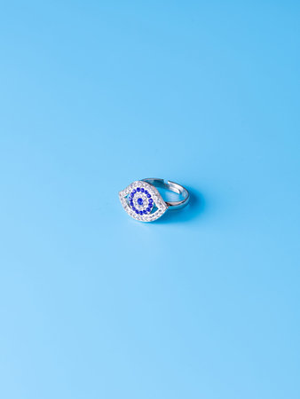 Close-up of a silver eye-shaped ring with white and blue rhinestones against a blue backgroundの写真素材