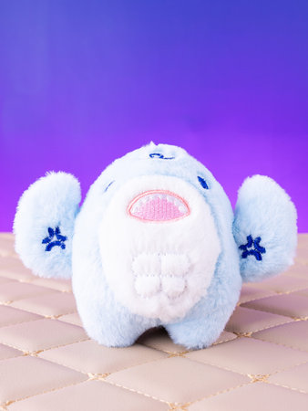 A close-up of a plush blue bag charm in the shape of a shark, placed on a leather surface.