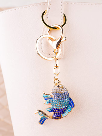 Close-up of a bright metal keychain in the shape of a blue fish made with rhinestones on a white bag