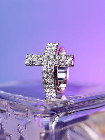 Close-up of a silver cross-shaped ring with white rhinestones on a purple backgroundの写真素材