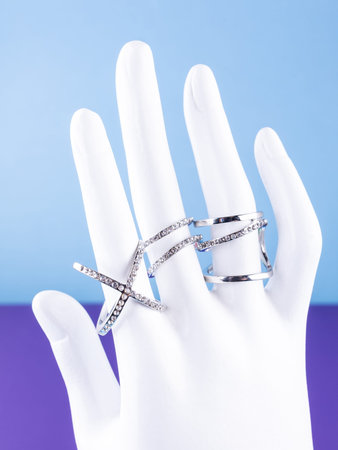 A close-up of a set of large white rings with rhinestones in a minimalist style on a white mannequin against a blue backgroundの写真素材