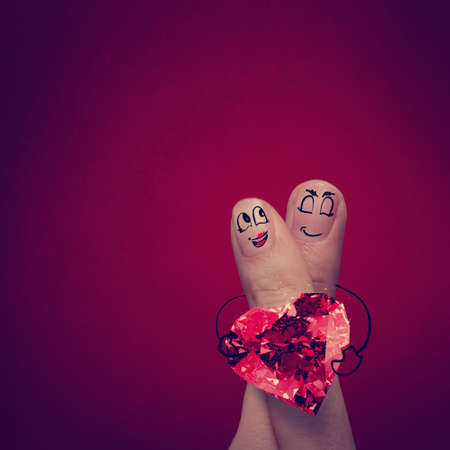 the happy finger couple in love with painted smiley and hold diamond ring heart shapeの写真素材