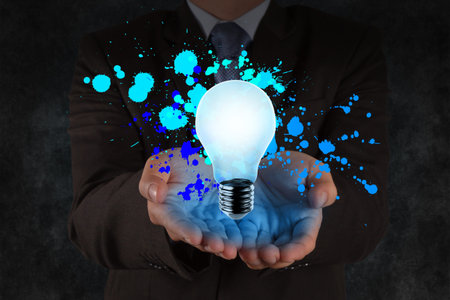 businessman hand shows light bulb and splash colors as creative conceptの写真素材