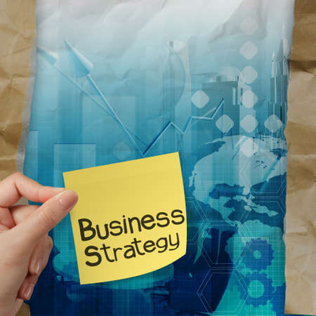 hand holds business strategy with sticky note on crumpled paper with tear envelope as conceptの写真素材