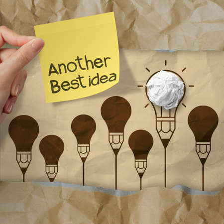 hand holding sticky note with another idea light bulb on crumpled paper as creative conceptの写真素材