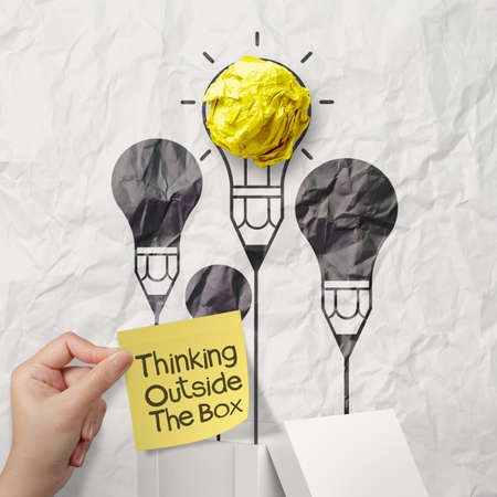 hand holds sticky note think outside the box on crumpled paper background as conceptの写真素材