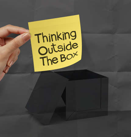 hand holding sticky note with thinking outside the box on dark crumpled paper as conceptの写真素材