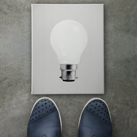 Hand drawn light bulb on dark canvas board front of business man feet as concept