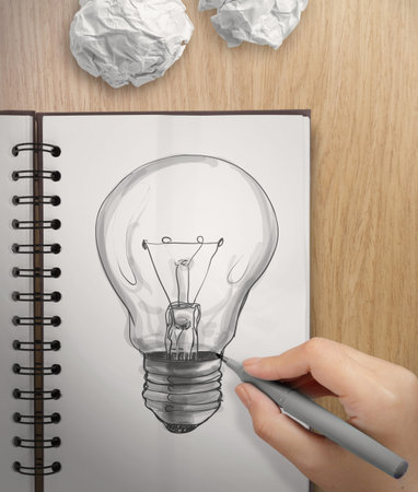 hand with a pen drawing light bulb on note book as conceptの写真素材