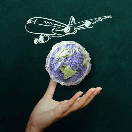 hand showing airplane with crumpled world paper symbol as concept on blackboardの写真素材