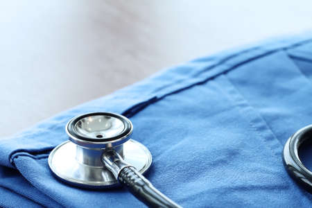 Stethoscope with blue doctor coat on wooden table with shallow DOF evenly matched and backgroundの写真素材
