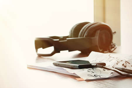 Closeup of smartphone with headphone on musical notes paper with shallow DOF evenly matched  on wooden deskの写真素材
