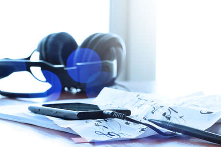Closeup of smart phone with headphone on musical notes paper with shallow DOF evenly matched on wooden deskの写真素材