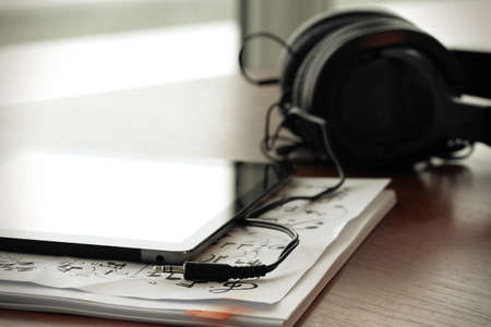 digital tablet with headphones on musical notes papers  with shallow DOF evenly matched and wooden deskの写真素材