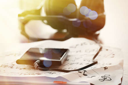 Closeup jack of smart phone with headphone on musical notes paper with shallow DOF evenly matched on wooden deskの写真素材