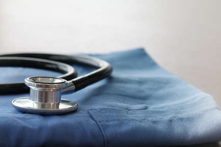 Stethoscope with blue doctor coat on wooden table with shallow DOF evenly matched and backgroundの写真素材