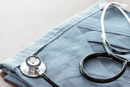 Stethoscope with blue doctor coat on wooden table with shallow DOF evenly matched and backgroundの写真素材
