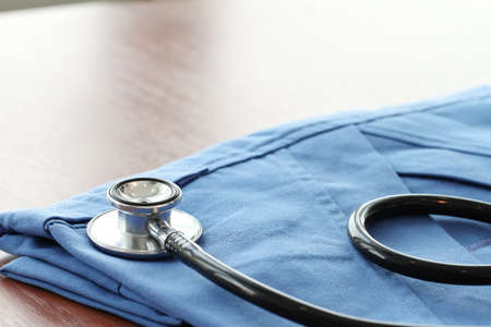 Stethoscope with blue doctor coat on wooden table with shallow DOF evenly matched and backgroundの写真素材