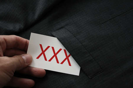 close up of businessman hand picking business card reading XXX from the pocket of gray suit jacket backgroundの写真素材