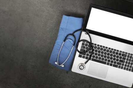 top view of workspace of medical with stethoscope and blue coat and blank screen computer laptop on texture desk backgroundの写真素材