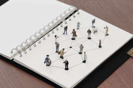 close up of miniature people with social network diagram on open notebook on wooden desk as social media coneptの写真素材