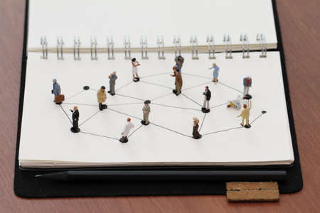 close up of miniature people with social network diagram on open notebook on wooden desk as social media coneptの写真素材