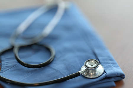 Stethoscope with blue doctor coat on wooden table with shallow DOF evenly matched and backgroundの写真素材