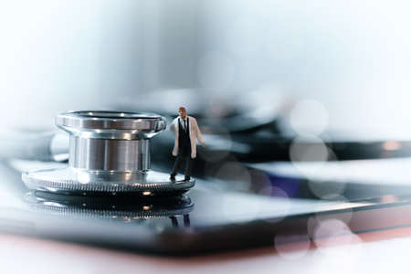 Modern medical concept- studio macro of miniature doctor with  a stethoscope and digital tablet  on wood table backgroundの写真素材